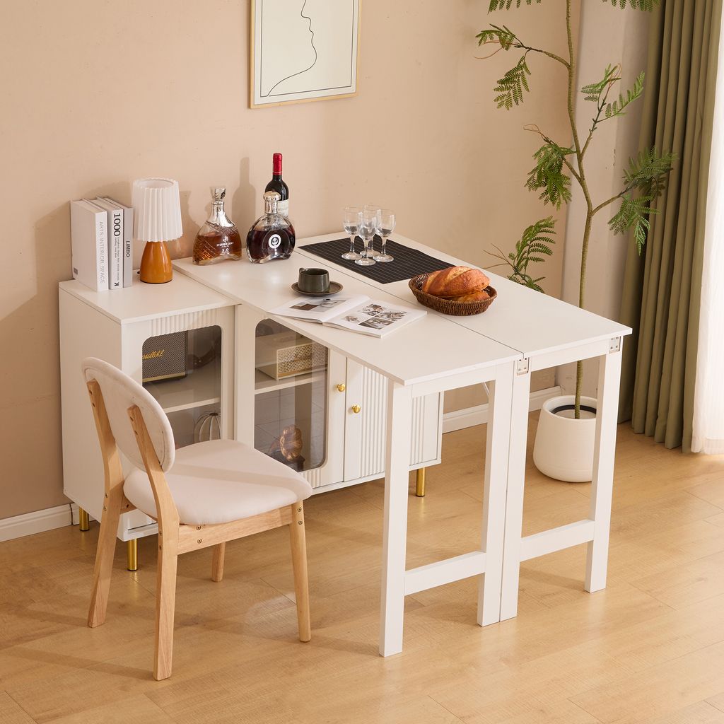 A white dining table with a built-in sideboard, set with wine, glasses, and bread, in a room with a plant and a chair.