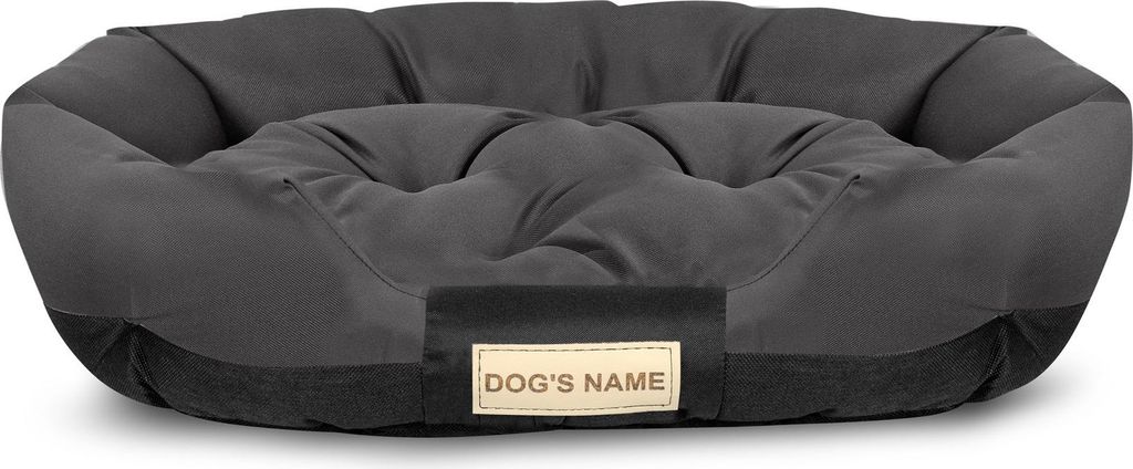 A dark gray dog bed with a lighter gray cushioned interior and a small beige tag with the words "DOG'S NAME" printed on it.