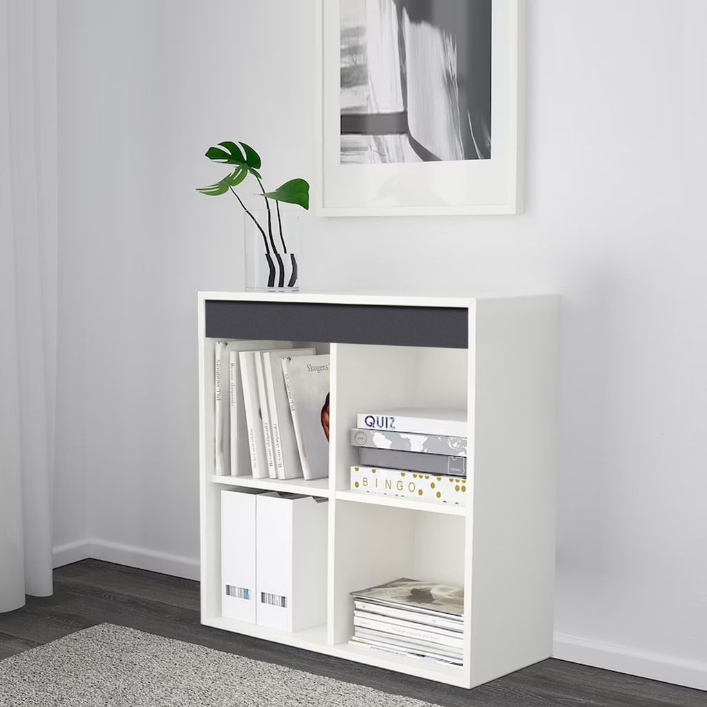 A white shelving unit with books and binders inside, placed against a white wall with a framed picture above.