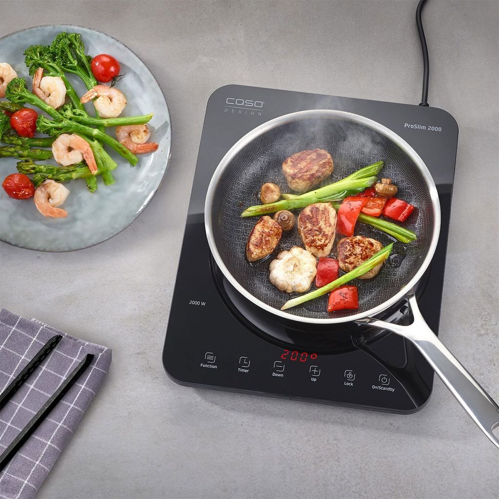 An induction cooktop with food cooking on it, placed next to a plate of cooked food.