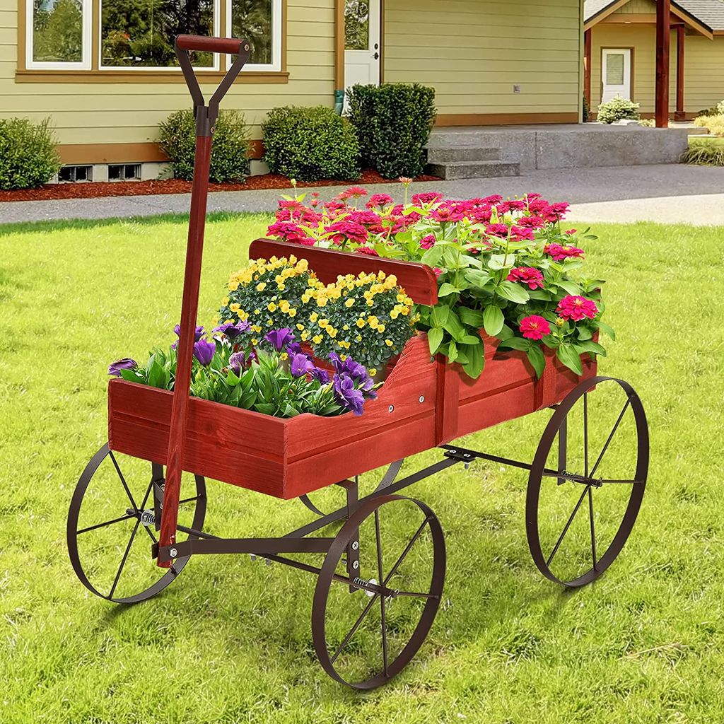 A red wooden wagon filled with colorful flowers sits on a green lawn in front of a house.
