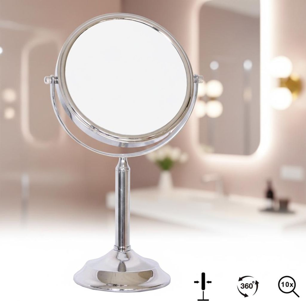 A silver vanity mirror on a stand, placed in a bathroom setting with blurred background elements.