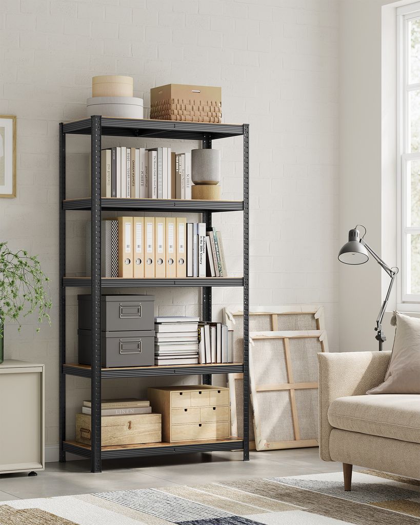 A storage shelf unit filled with books and boxes in a room with a sofa and a window.
