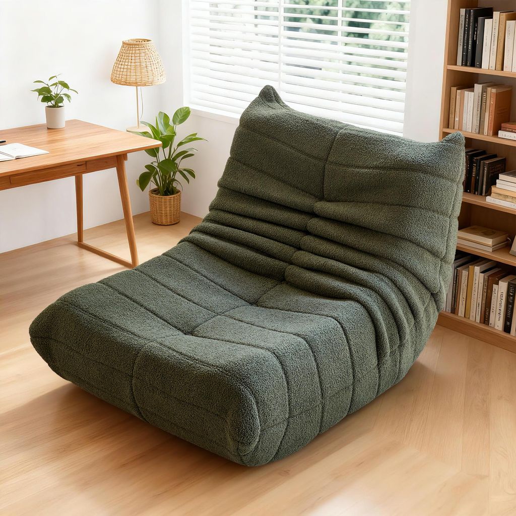 A green sofa is placed in a room with a wooden desk and a bookshelf.