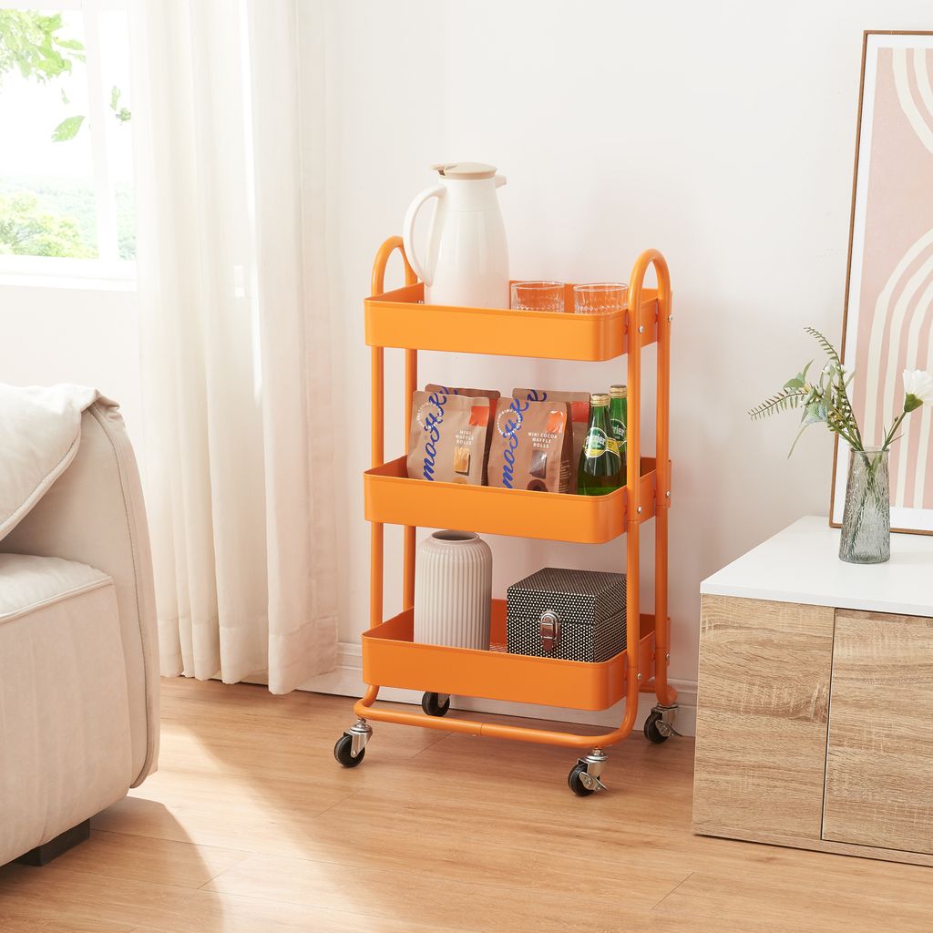 An orange kitchen trolley with three shelves is shown in a room with a sofa and a cabinet.