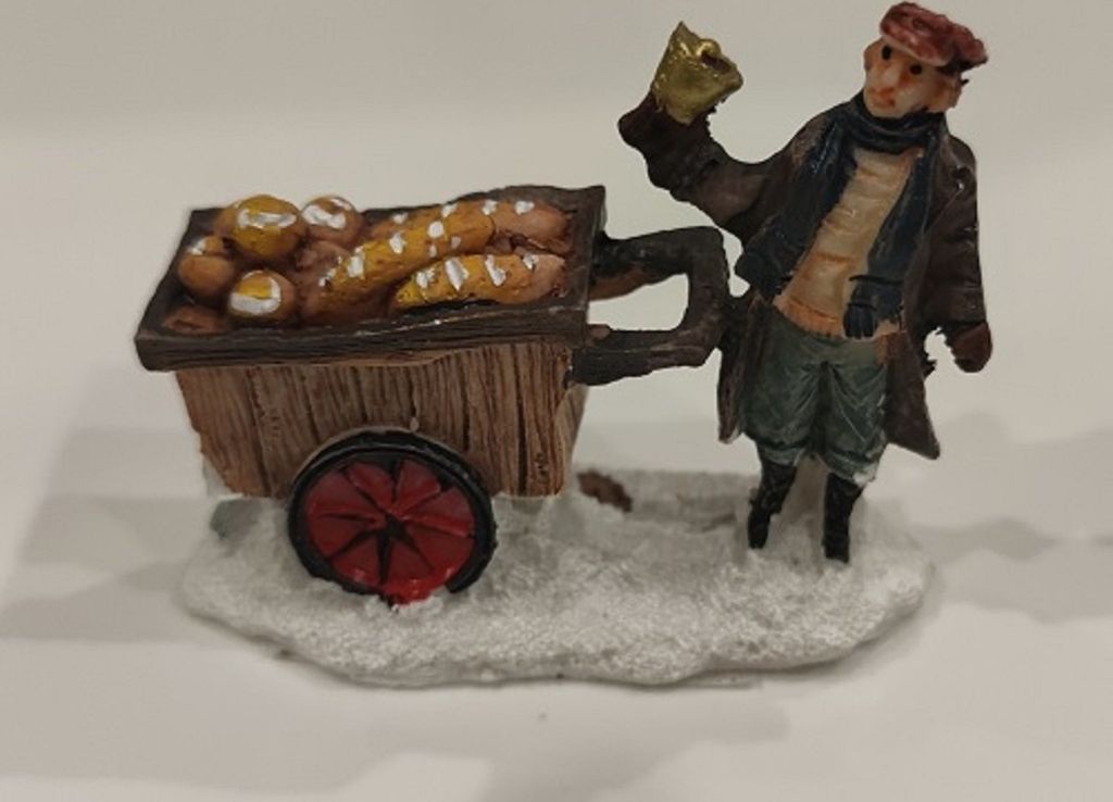 Eine kleine Figur, die einen Bäcker darstellt, der einen Karren voller Brot und Brötchen zieht.