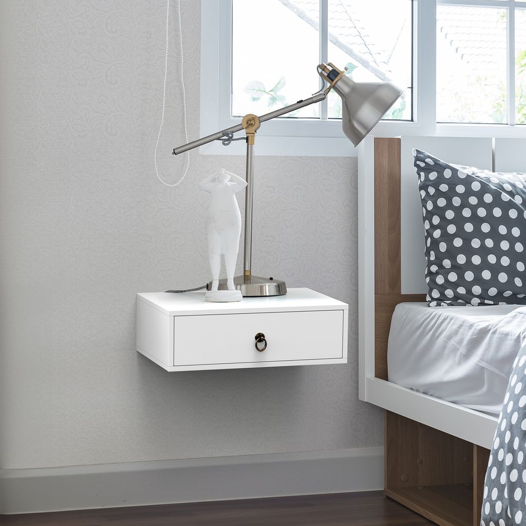 A white floating nightstand with a drawer next to a bed with a polka dot pillow.