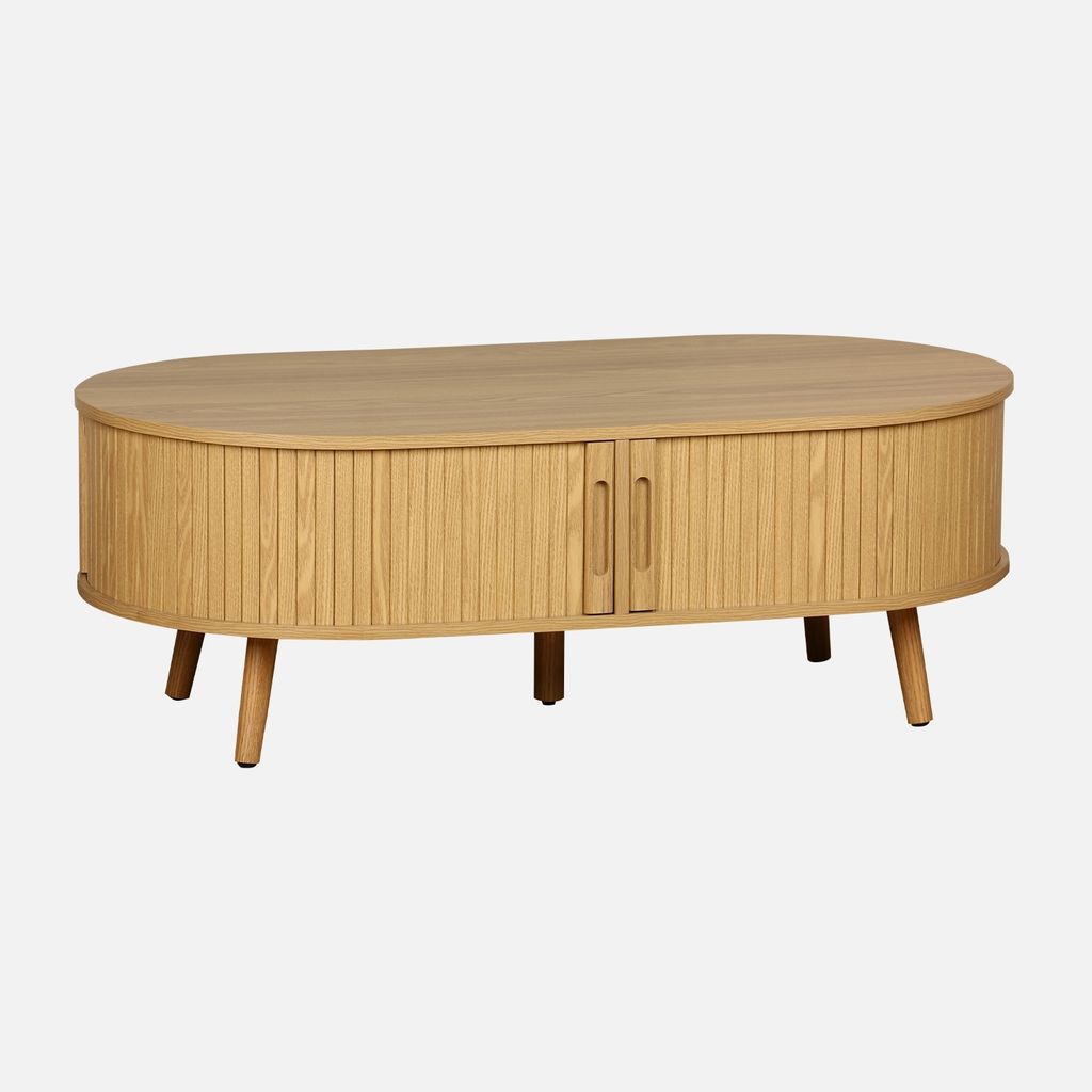 A light brown, oval-shaped coffee table with fluted sides and two doors, shown from the front on a plain background.