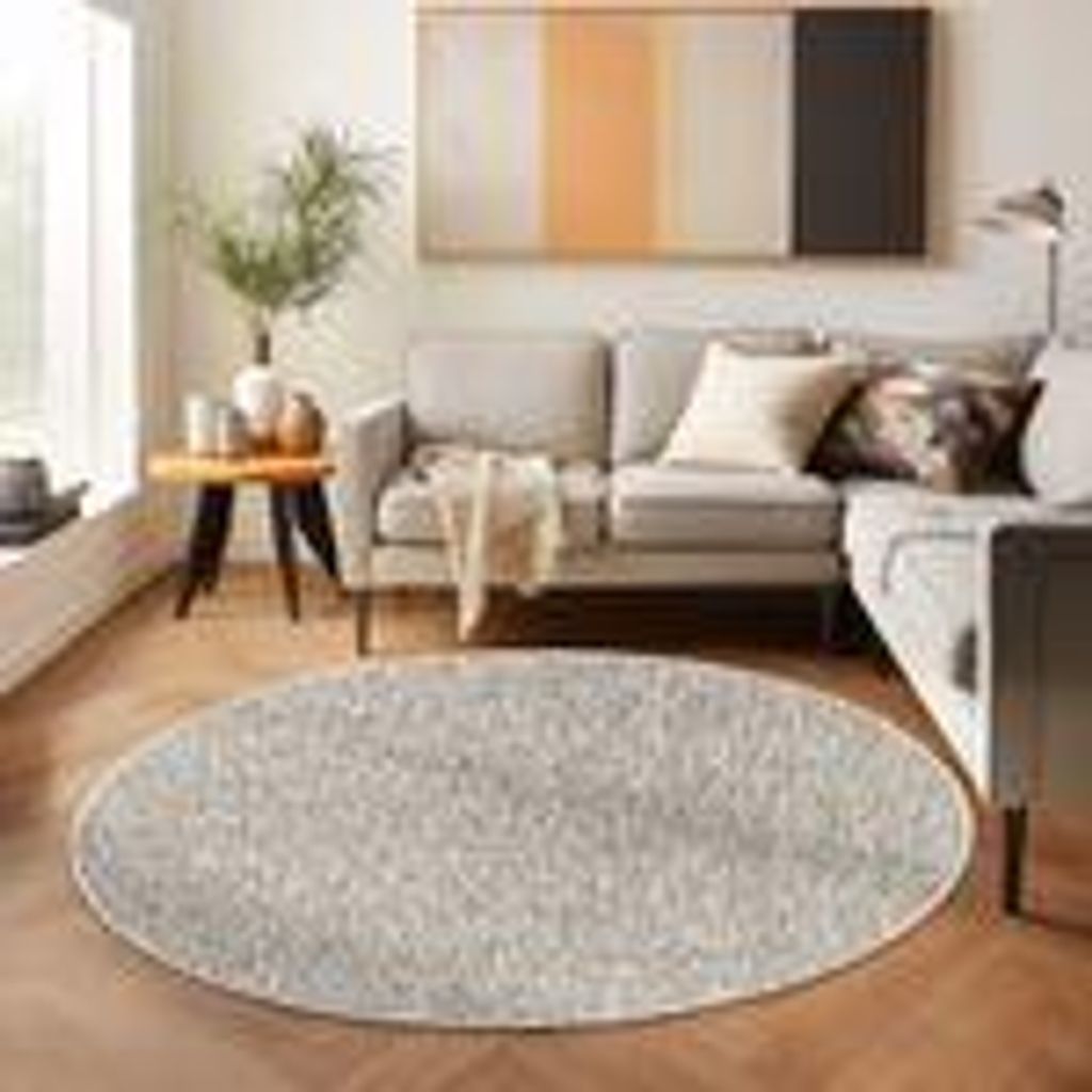 A circular rug is placed on a wooden floor in front of a sofa in a living room.