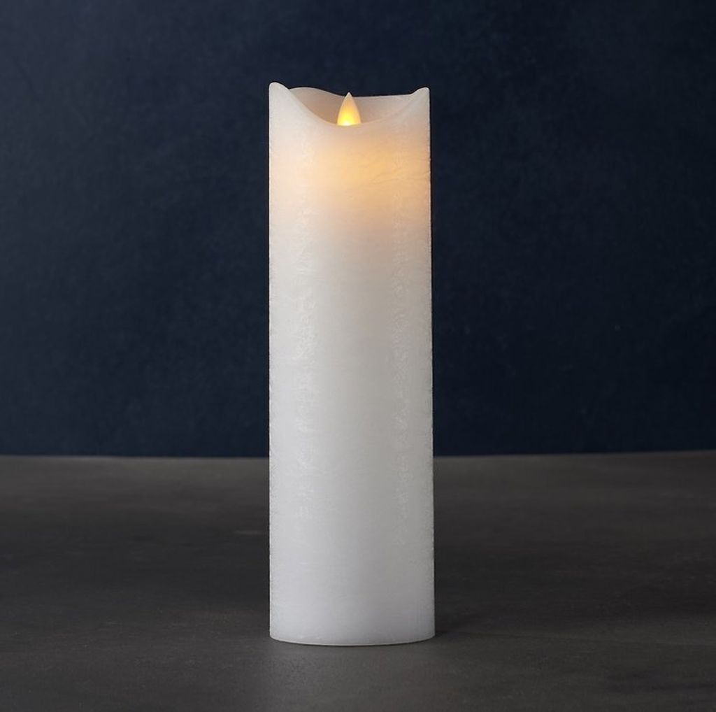 A white LED candle with a flickering flame sits on a dark surface against a dark blue background.