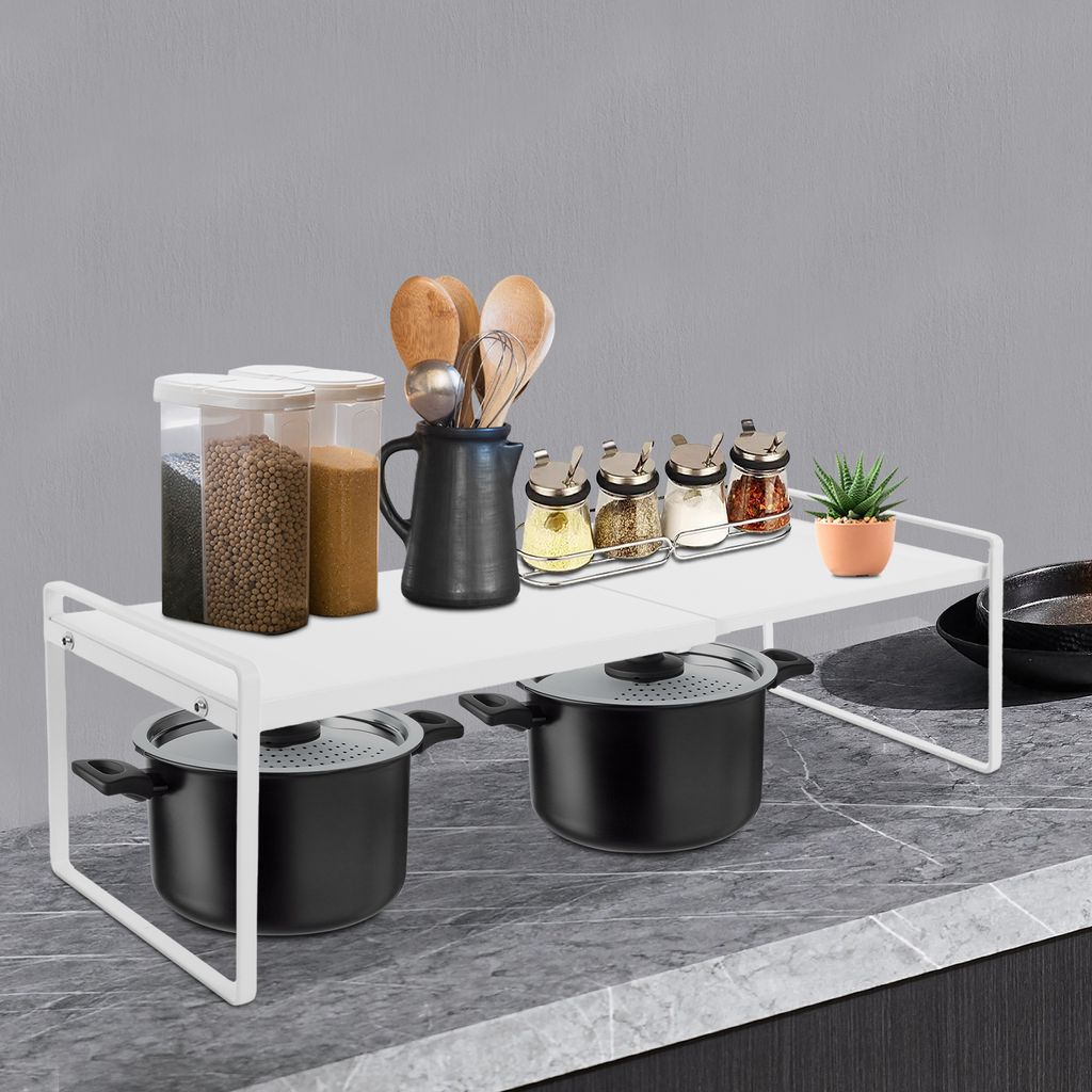 A white metal shelf unit is placed on a countertop, holding kitchen items like spice jars, utensils, and pots.
