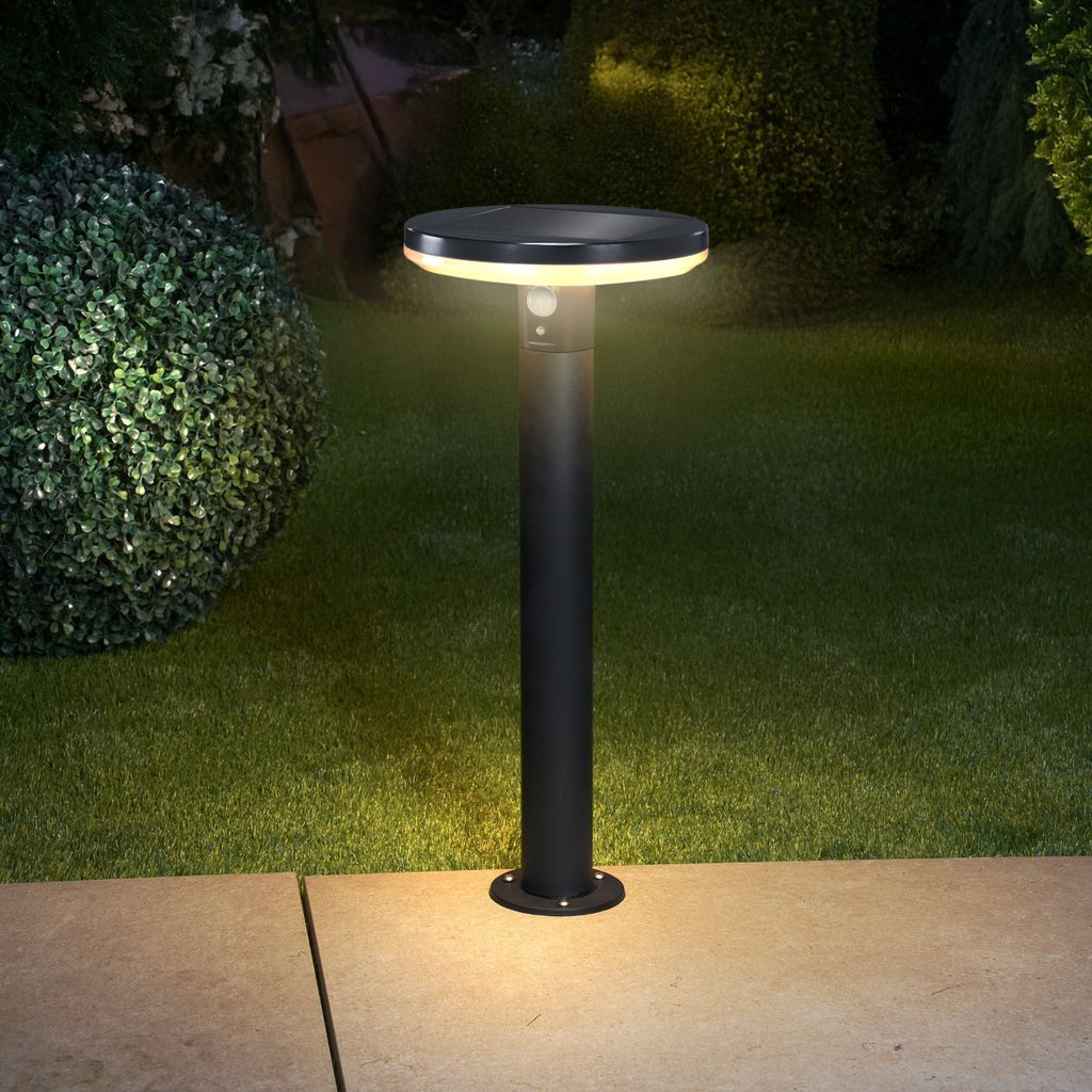 A solar-powered garden light illuminates a lawn and pathway at night.