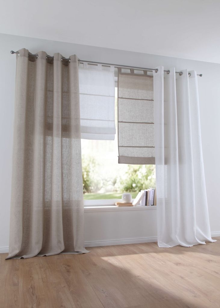 A window with multiple curtains and roman blinds, overlooking a garden.