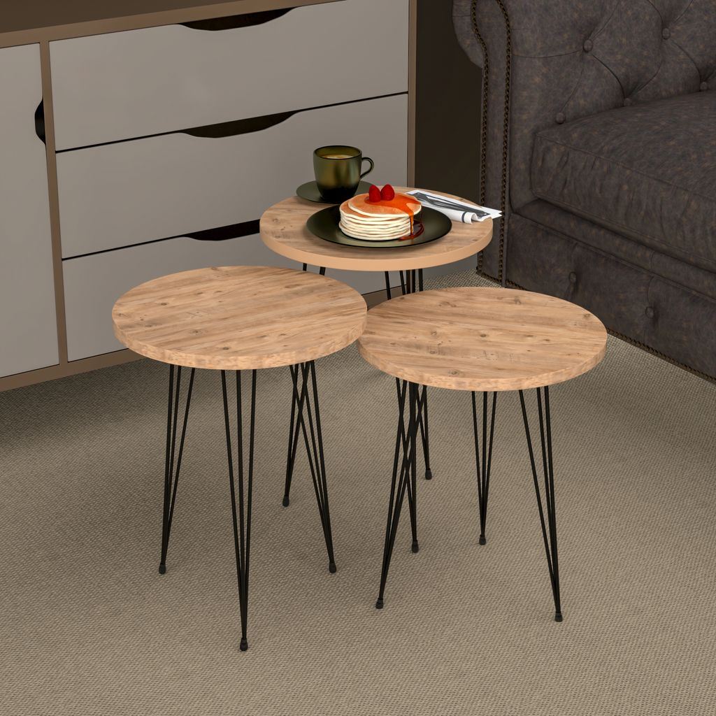 A set of three round nesting tables with wooden tops and black metal legs are arranged on a carpeted floor next to a sofa and a dresser. One of the tables has pancakes and a cup of coffee on it.