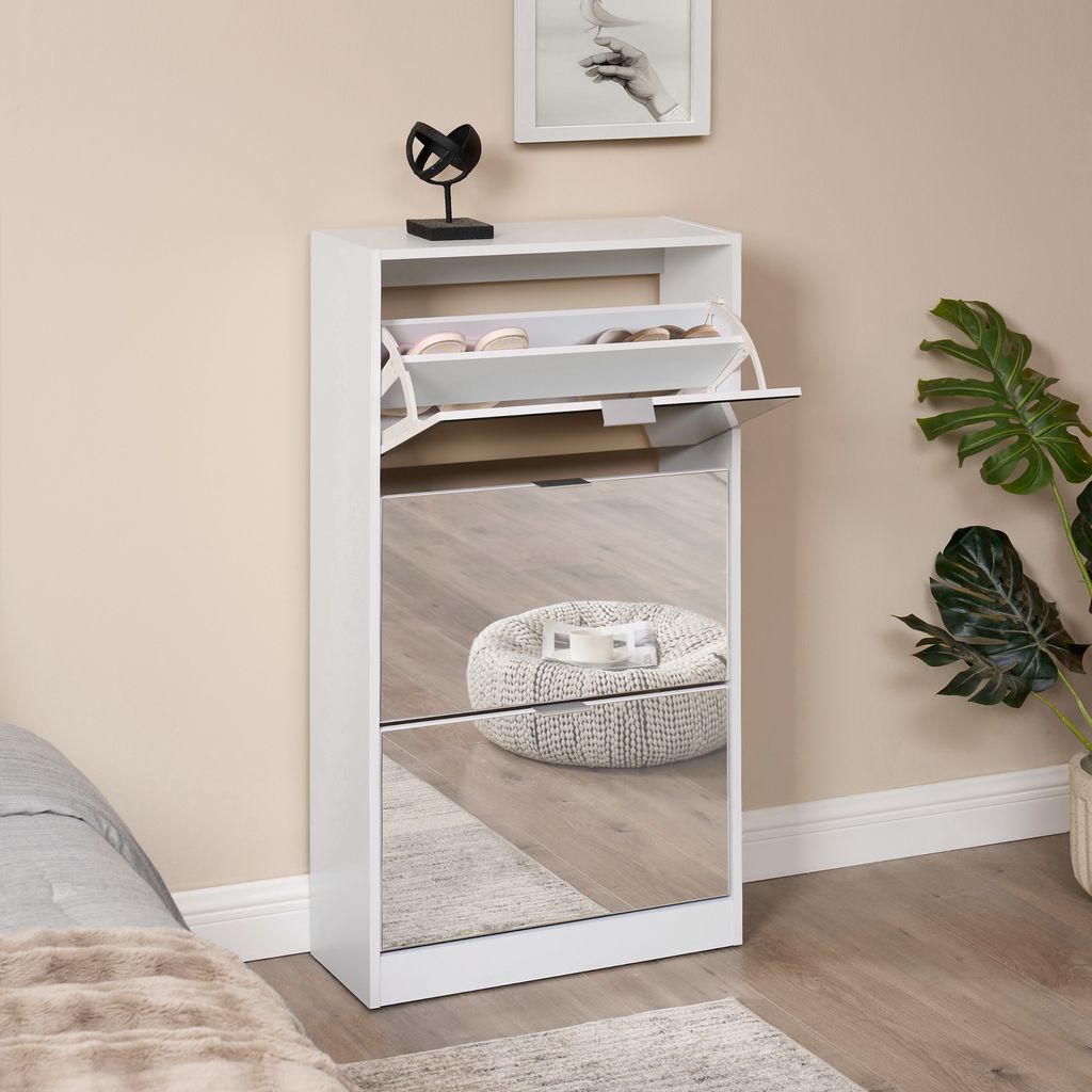 A white shoe cabinet with mirrored doors is shown in a room setting, next to a bed and a plant.