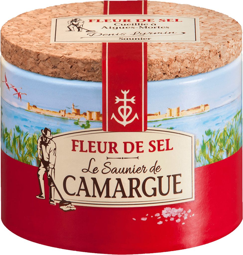 A round tin of Fleur de Sel with a scenic illustration of a coastal town and a salt harvester.