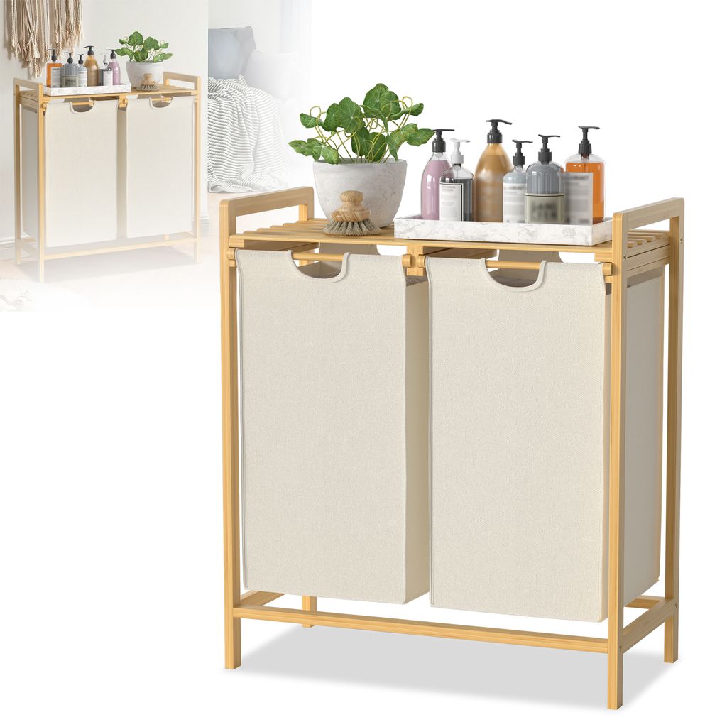 A two-compartment laundry basket with a bamboo frame and a shelf on top, displayed against a white background. Several bottles of soap and a potted plant are arranged on the shelf.