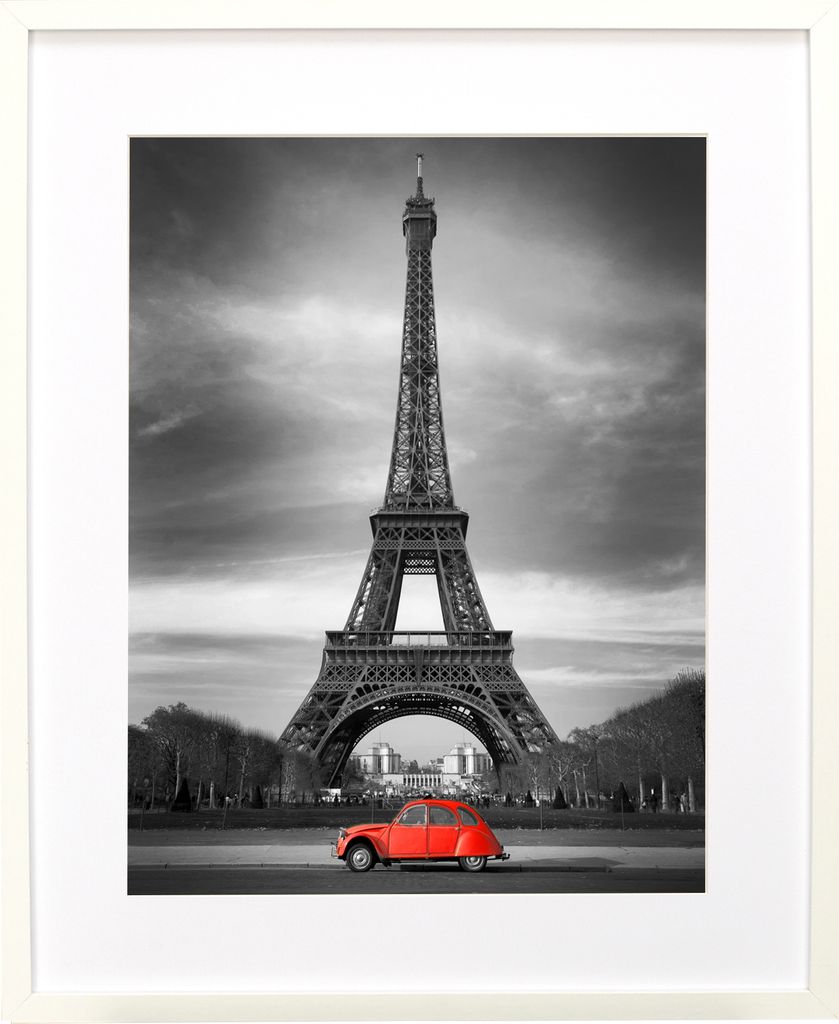 A framed black and white photograph of the Eiffel Tower with a red car in the foreground.