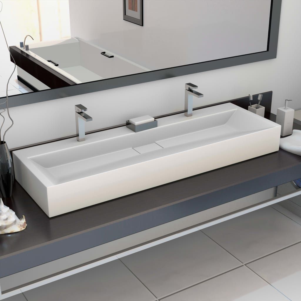 A modern bathroom sink with two faucets reflected in a mirror.