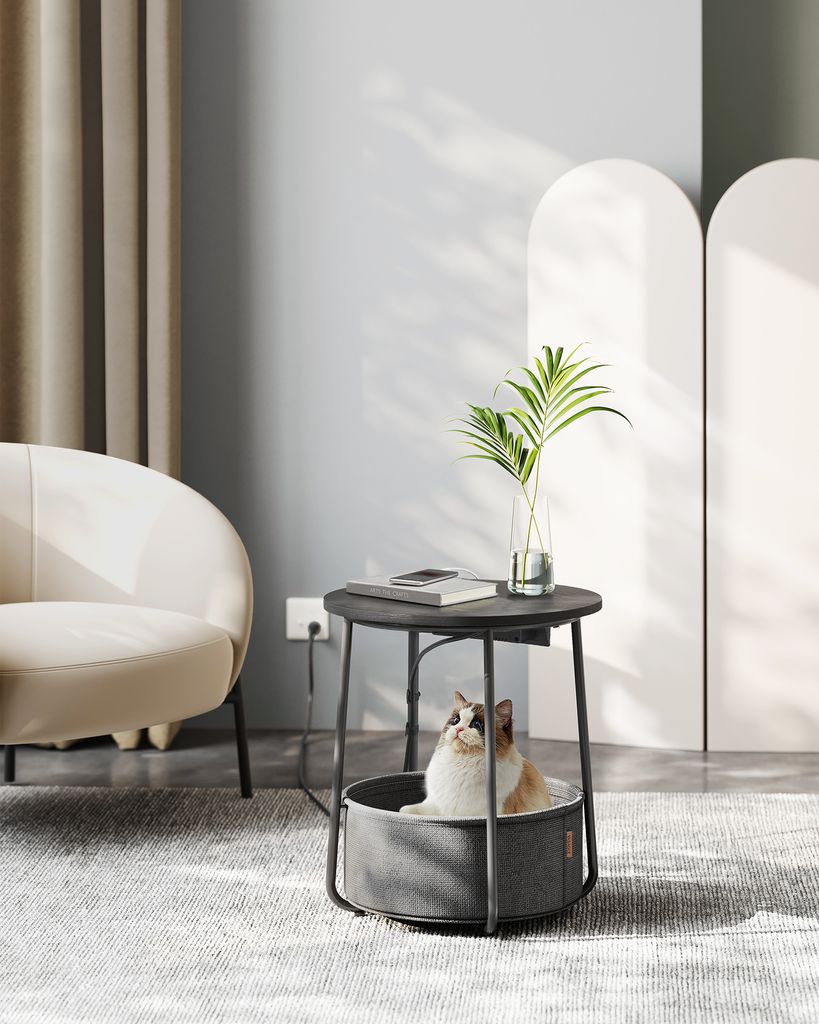 A cat sits in a pet bed integrated into a round side table in a living room setting.