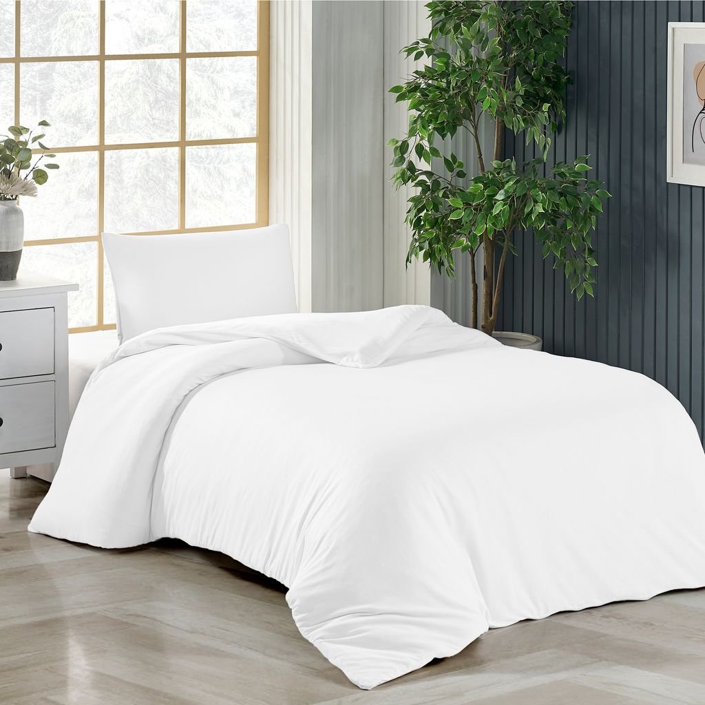 A white duvet and pillow set on a bed, with a large window and a plant in the background.