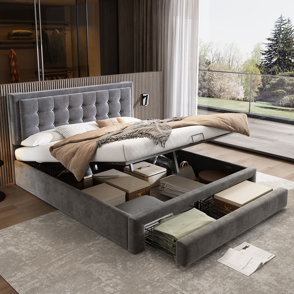 A modern bedroom with a large storage bed, open to reveal storage compartments. Large windows show a garden view.