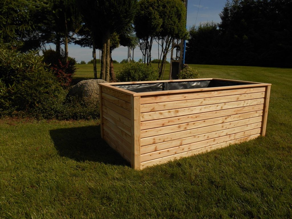 A wooden raised garden bed sits on a grassy lawn with trees and bushes in the background.