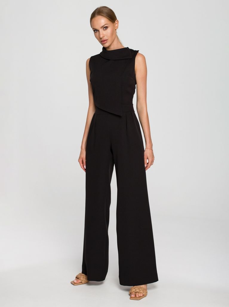 A woman wearing a black jumpsuit stands against a white background.