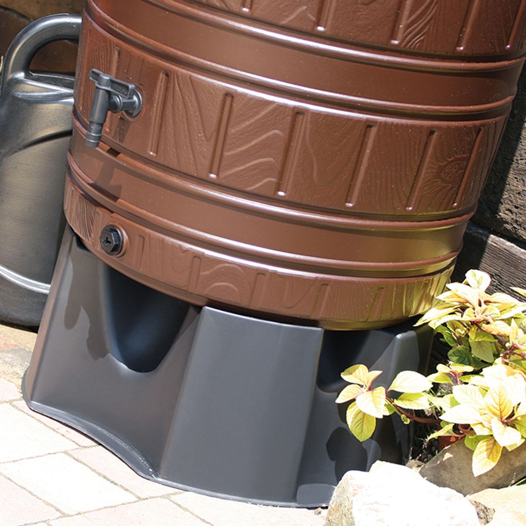 A close-up view of a brown rain barrel stand with a watering can in the background.