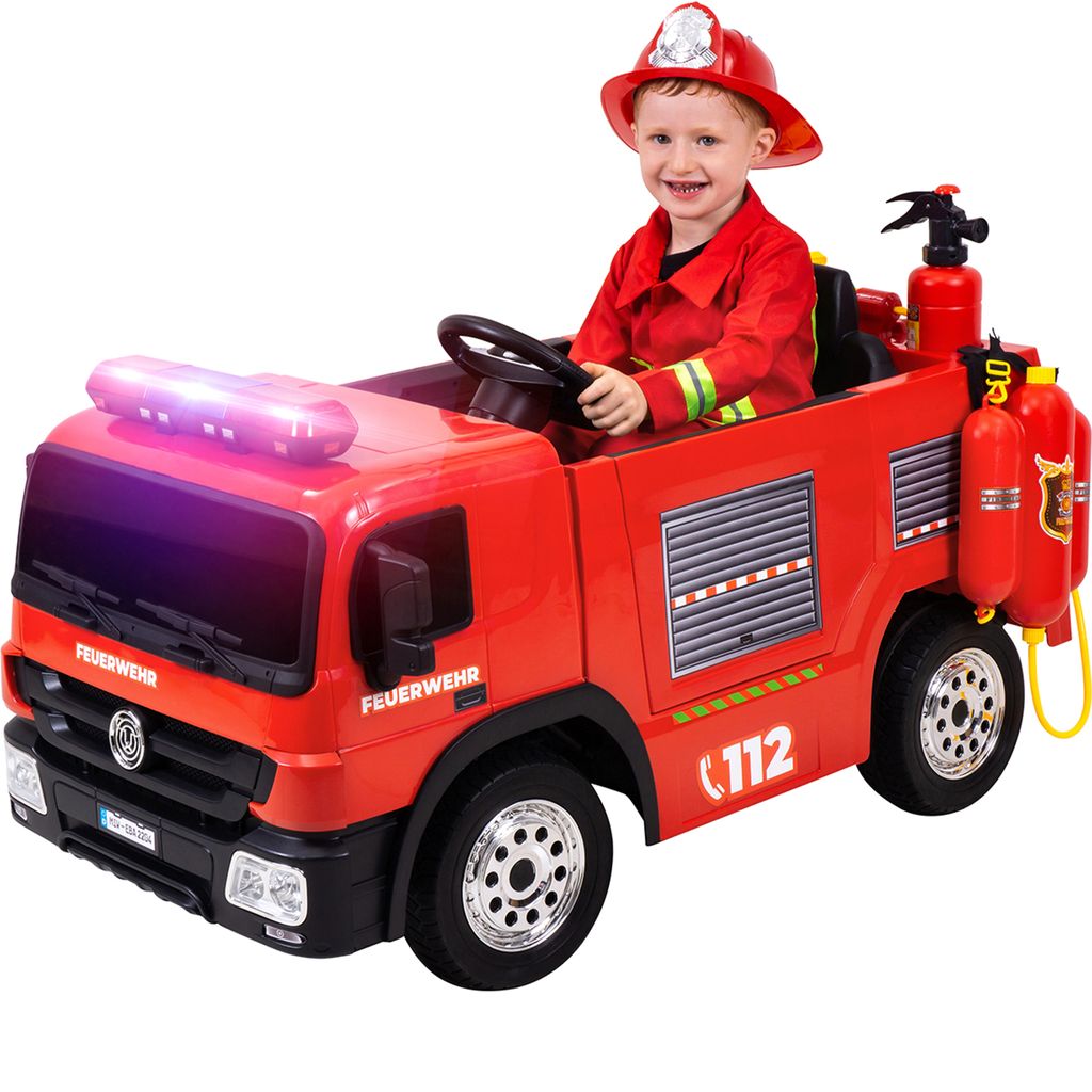 A child dressed as a firefighter is sitting in a toy fire truck.