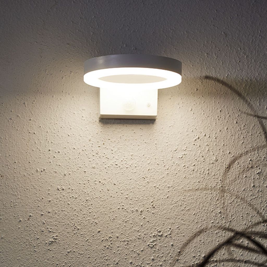 A modern white wall-mounted light fixture with a circular top and a rectangular base.