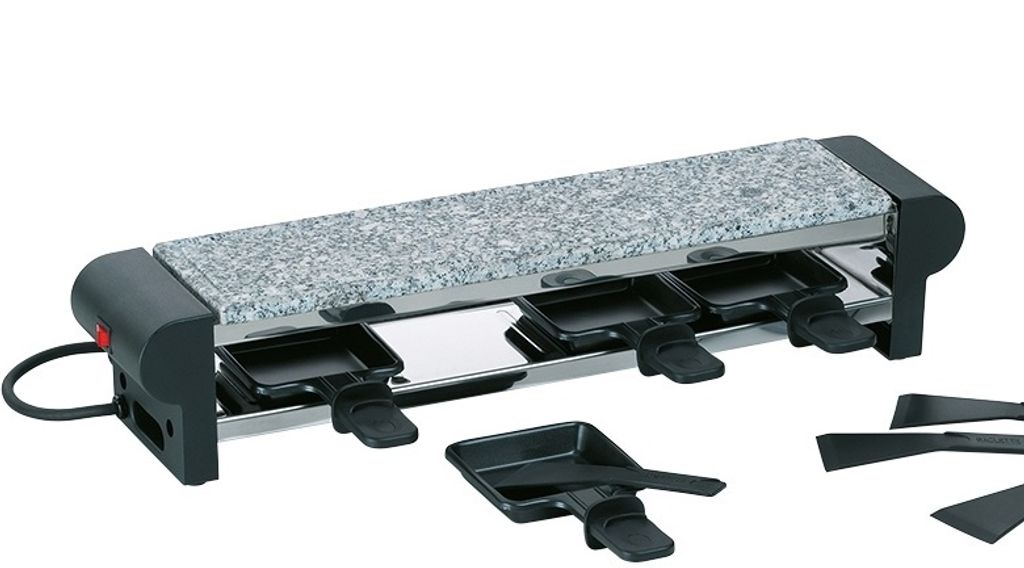 A raclette grill with a stone top and four individual cooking pans underneath, along with several spatulas.