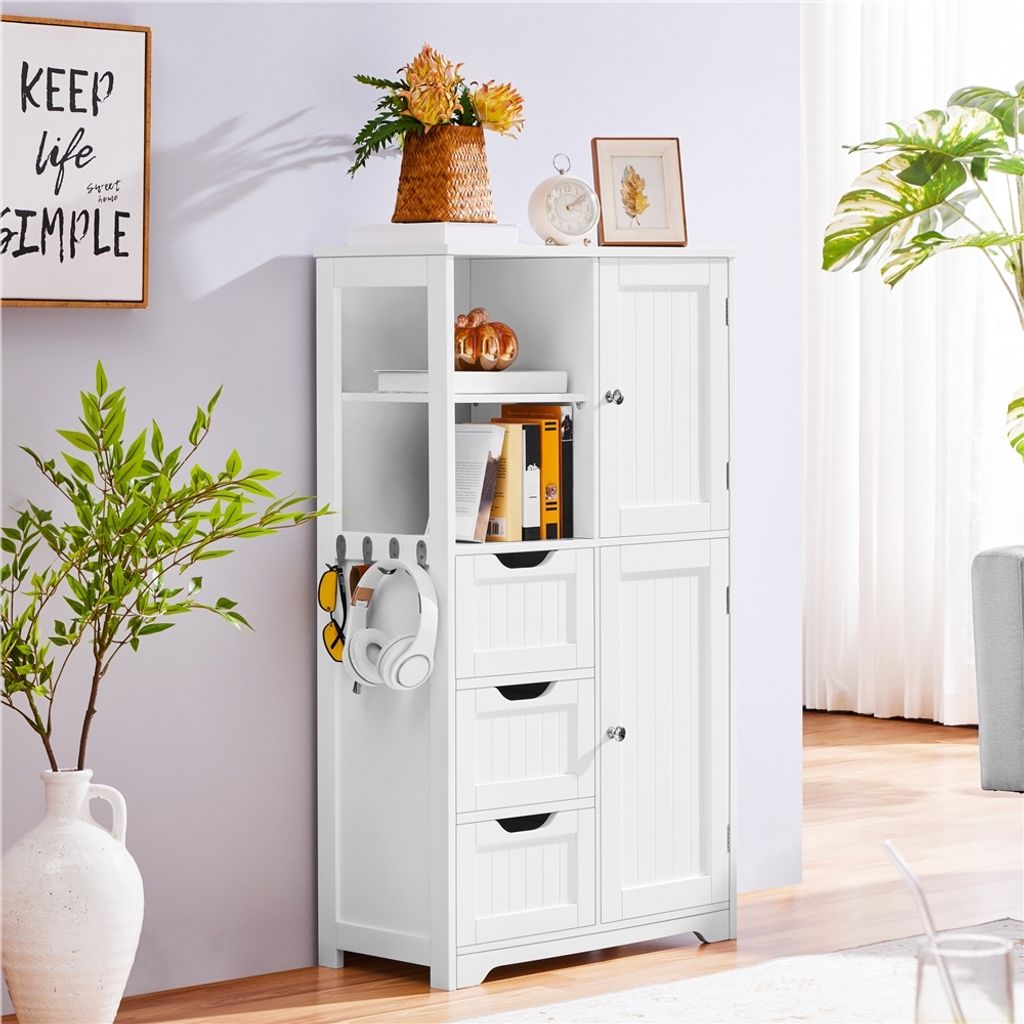 A white storage cabinet with shelves, drawers, and doors, decorated with a vase of flowers, a framed picture, and a clock on top. A plant is visible to the right.