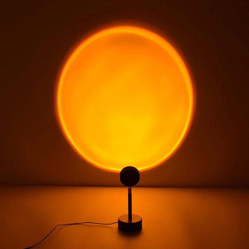 A sunset lamp projects a large orange circle onto a wall, with the lamp itself visible in the foreground.