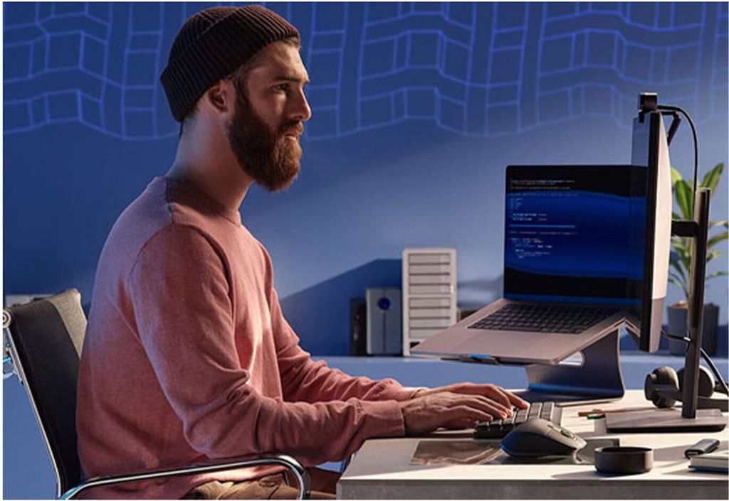 A man is working on a laptop in a dimly lit room with blue walls.