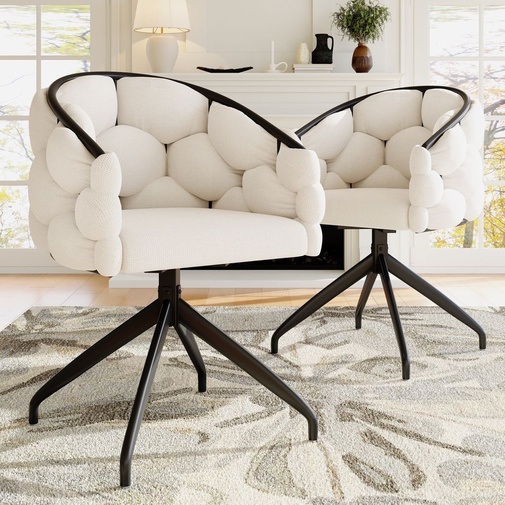 Two beige upholstered chairs with black metal legs are placed on a patterned rug in a living room setting, with a fireplace and window in the background.