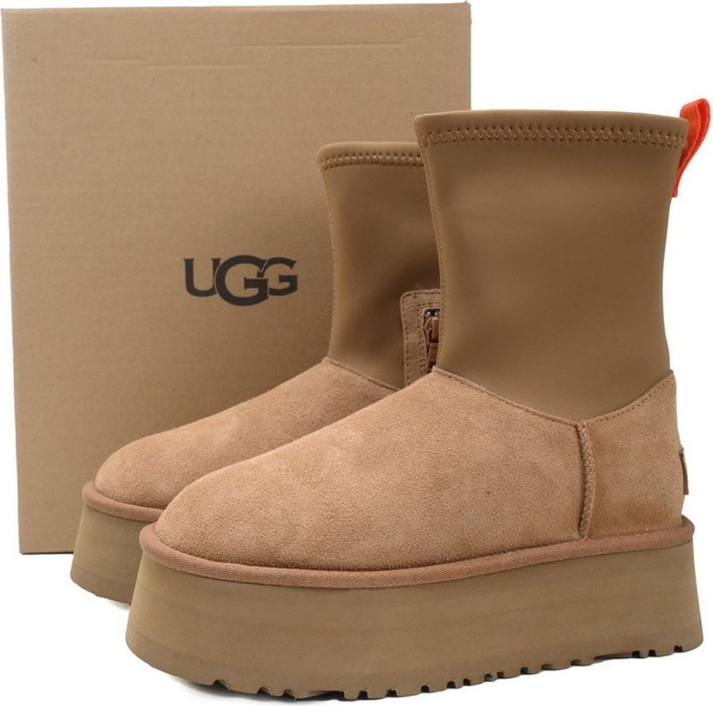 A pair of brown UGG boots with a platform sole and a cardboard UGG box in the background.