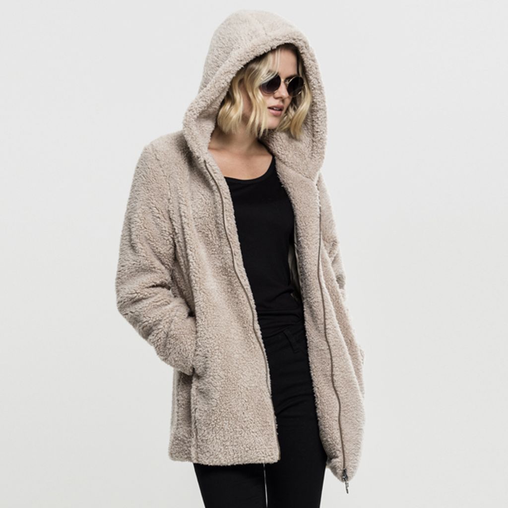 A woman wearing a beige sherpa jacket and sunglasses, posing against a white background.