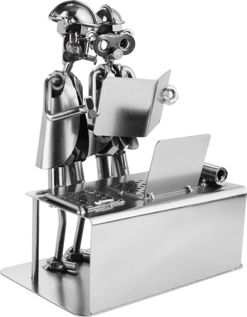 A metal figurine of two engineers looking at a book and a laptop on a desk.