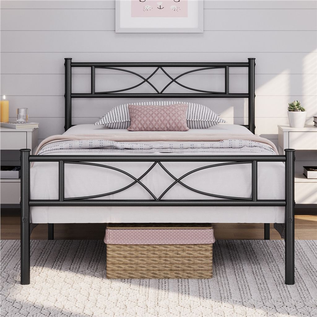 A black metal bed frame with a decorative headboard and footboard, set up in a bedroom with bedding and pillows.