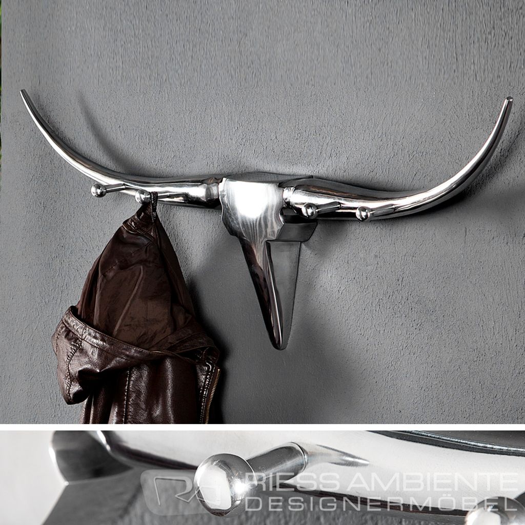 A metallic bull head coat rack mounted on a gray wall with a brown leather jacket hanging on it. The bottom part of the image shows a close-up of a shiny metallic surface with text.