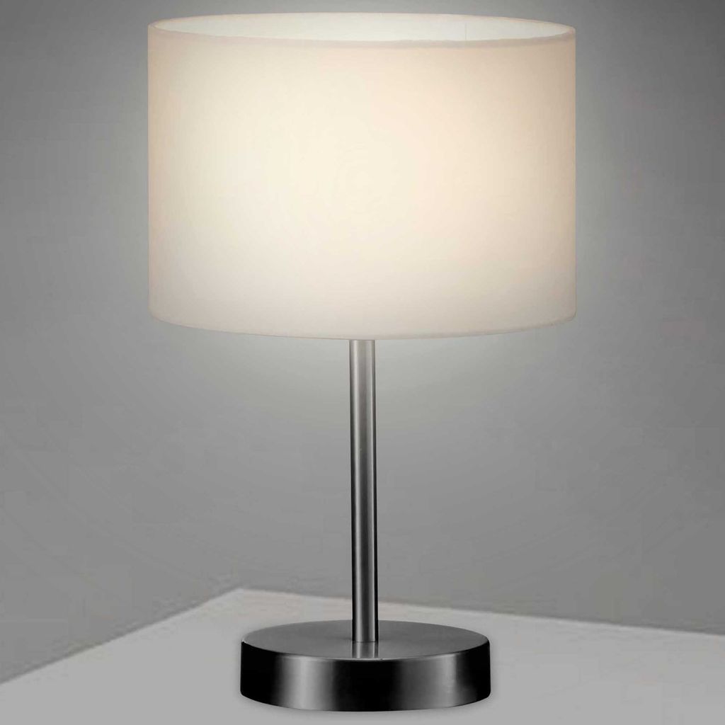 A table lamp with a white cylindrical shade and a silver metallic base and stem, placed on a white surface against a light gray background.