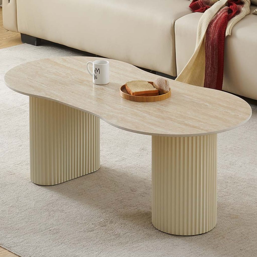 A modern coffee table with a travertine-look top and fluted cylindrical legs, placed on a rug in a living room setting.