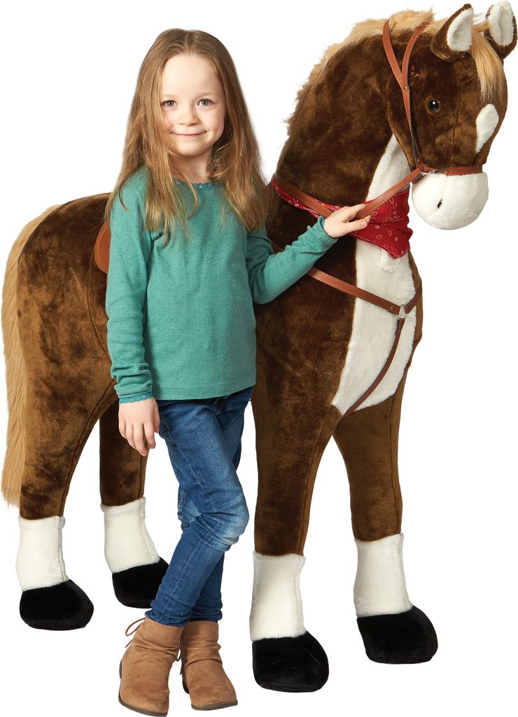 A young girl stands next to a large plush horse toy.