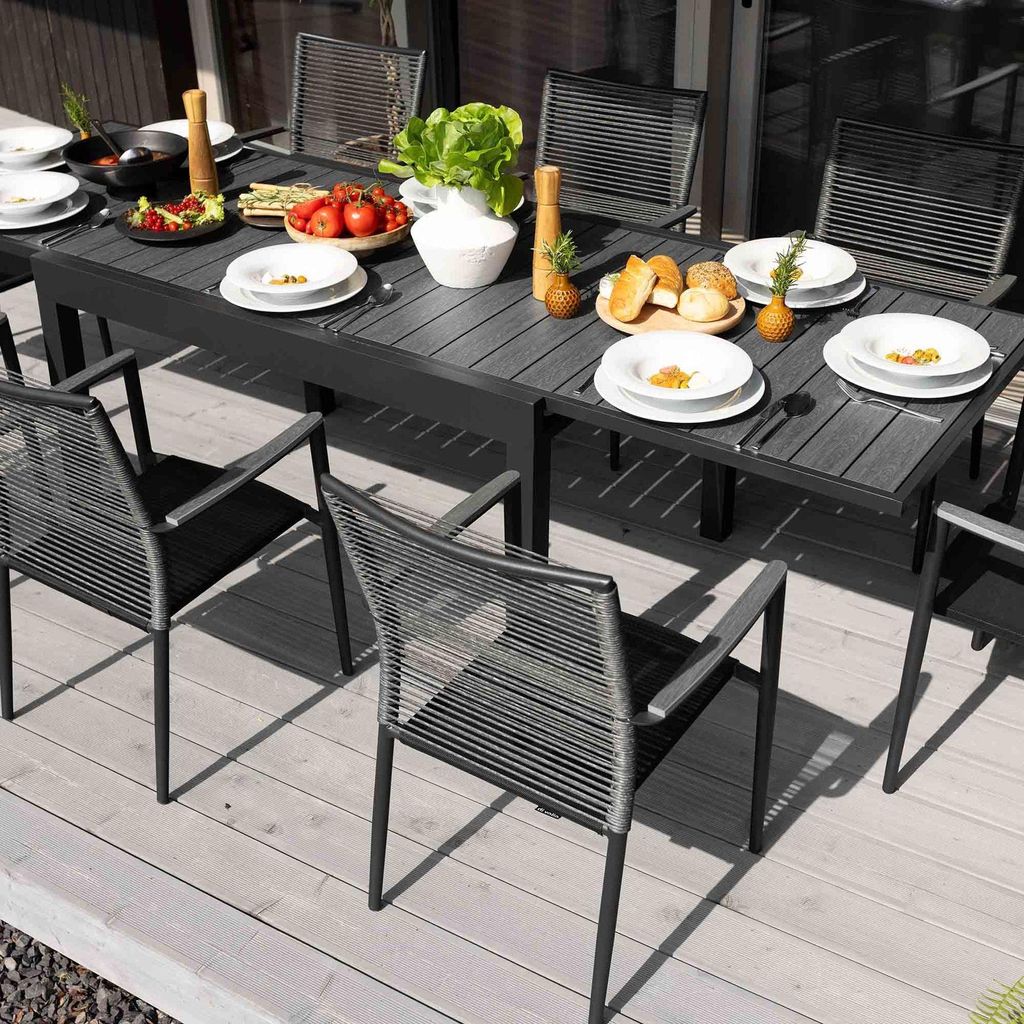 An outdoor dining set with a table and chairs, set up on a wooden deck with food and drinks on the table.