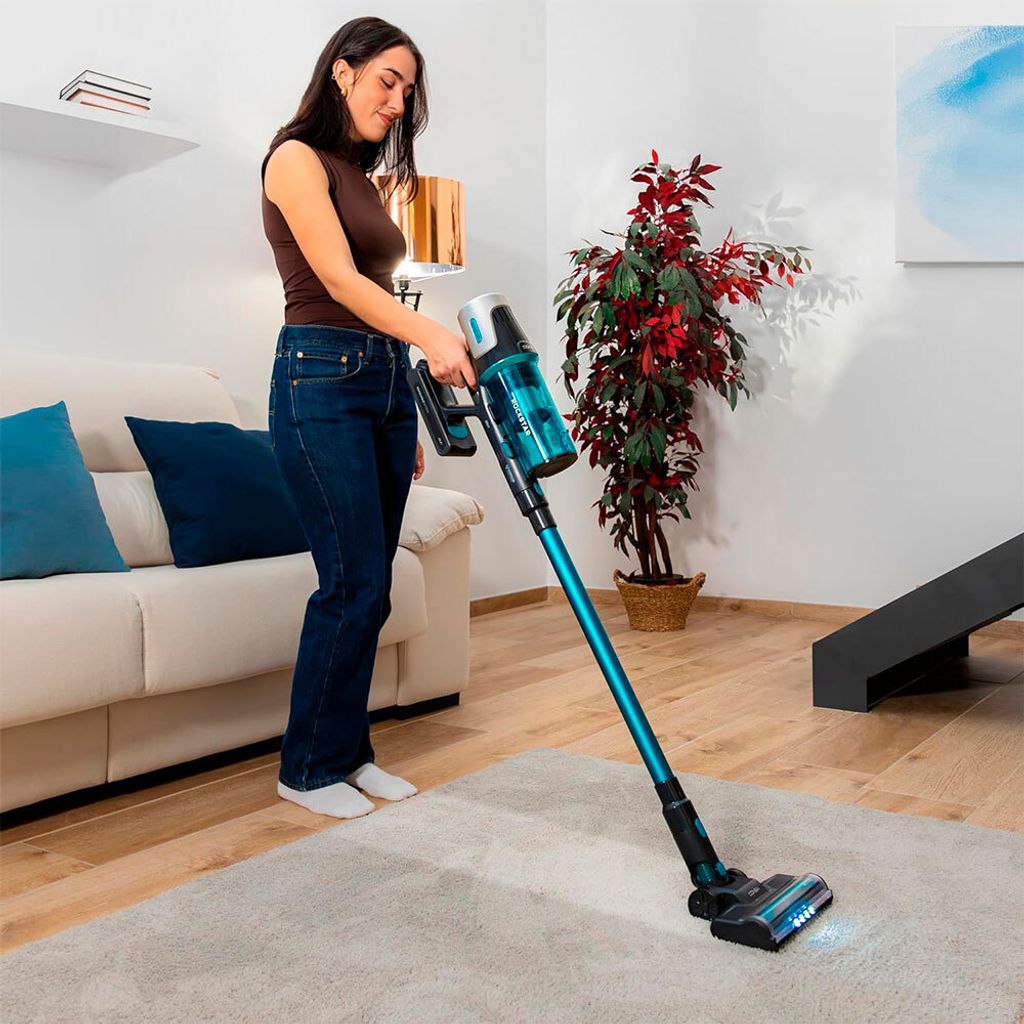 A woman is vacuuming a rug in a living room with a cordless vacuum cleaner.