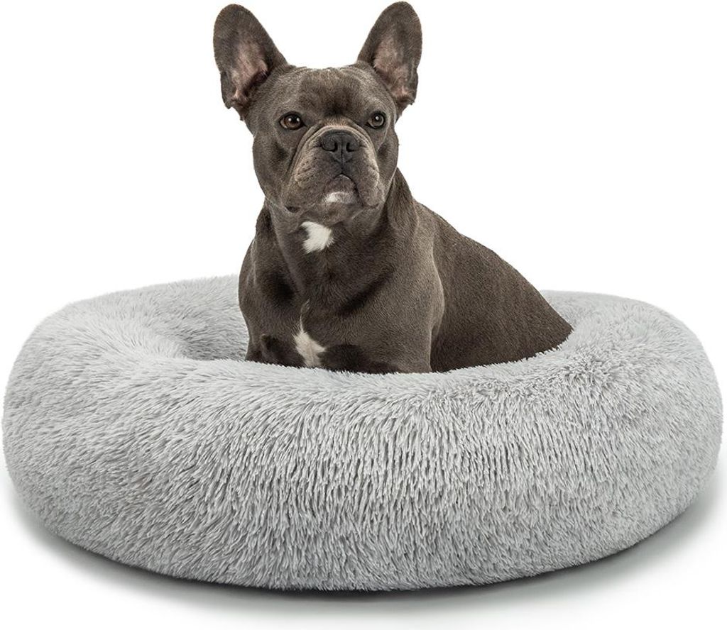 A French Bulldog sits in a round, plush dog bed.