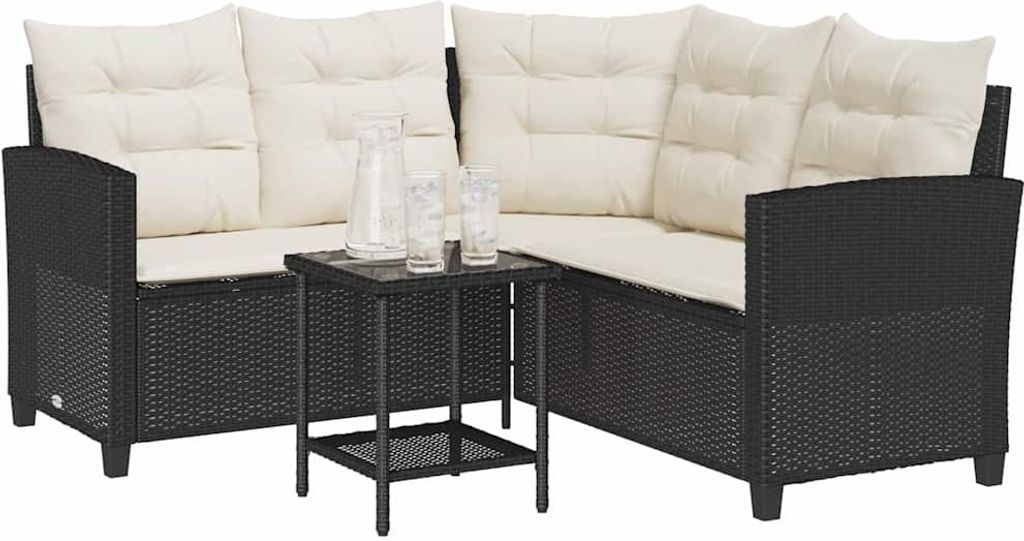 A black poly rattan L-shaped sofa with cream cushions and a small black coffee table with two glasses and a pitcher on it, set against a white background.