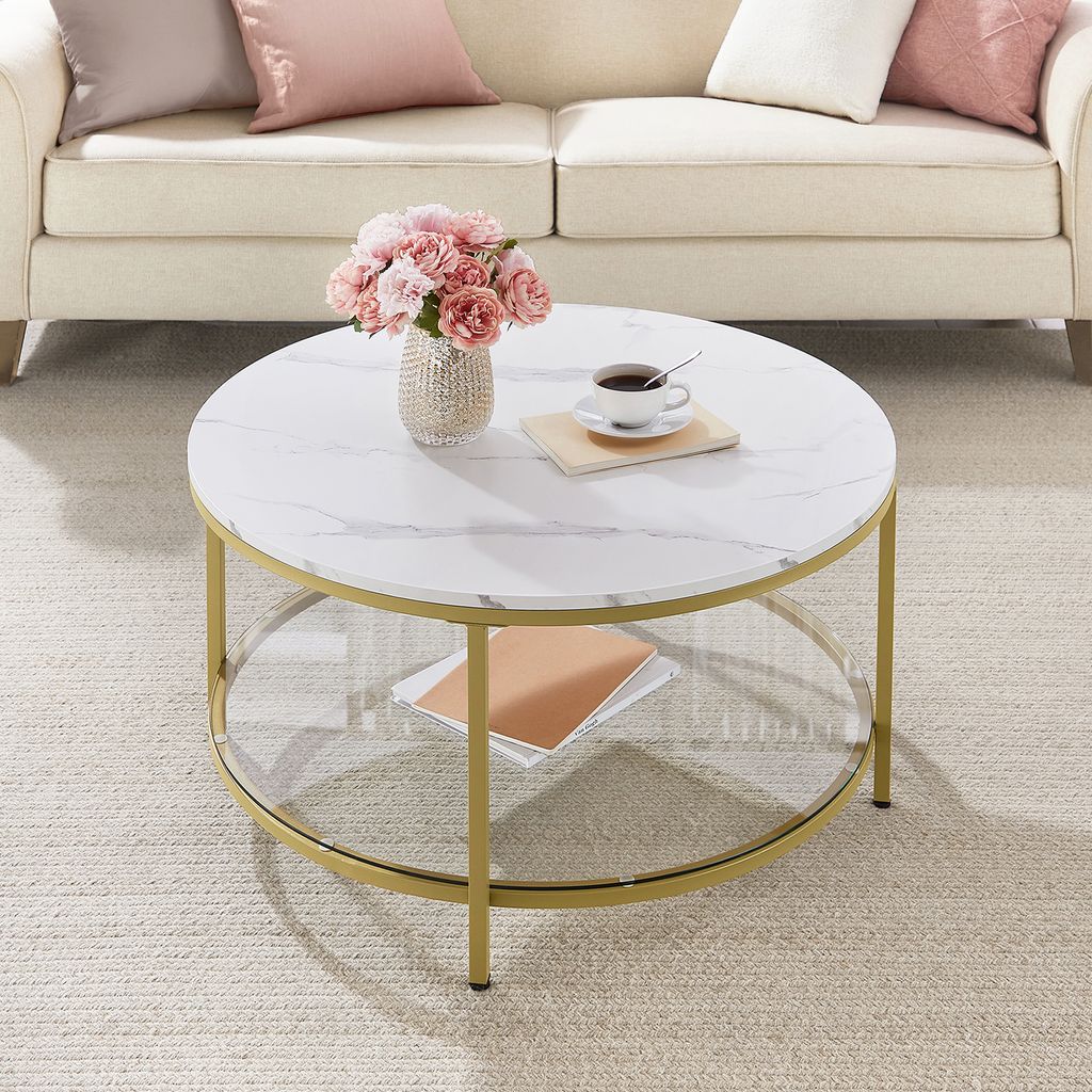 A coffee table with a marble top and gold legs is placed in a living room setting with a sofa and pillows.