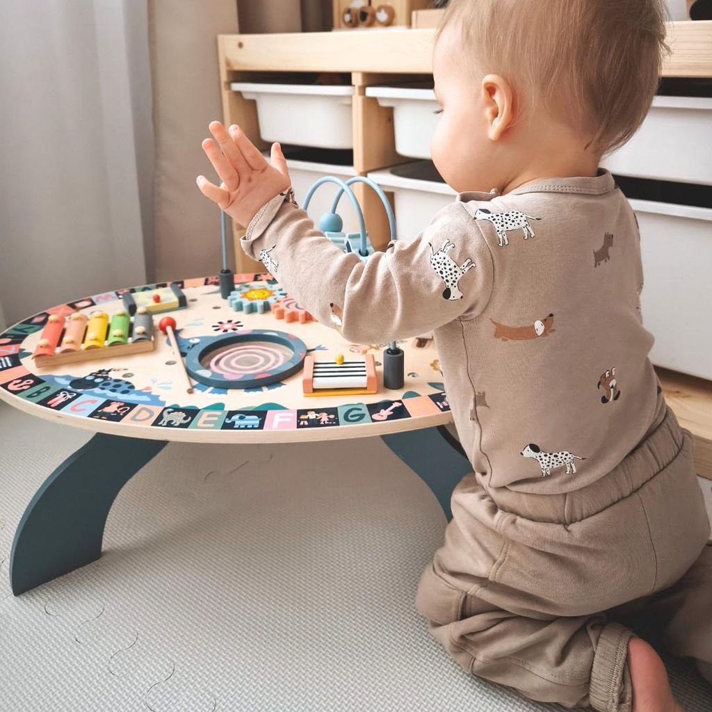 A baby is playing with a colorful wooden activity table.